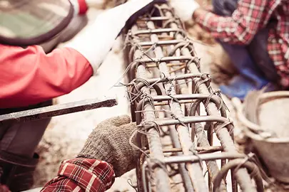 Bauarbeiter mit Schutzhandschuhen flechten Bewehrungsstahl für ein Betonfundament auf einer Baustelle.