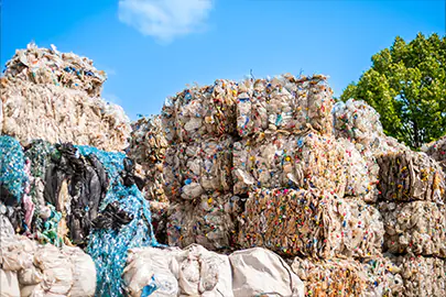 Große, ordentlich aufgestapelte Ballen aus gepresstem Kunststoffmüll und bunten PET-Flaschen auf dem Außengelände eines Recyclingunternehmens in Dresden, Sachsen.